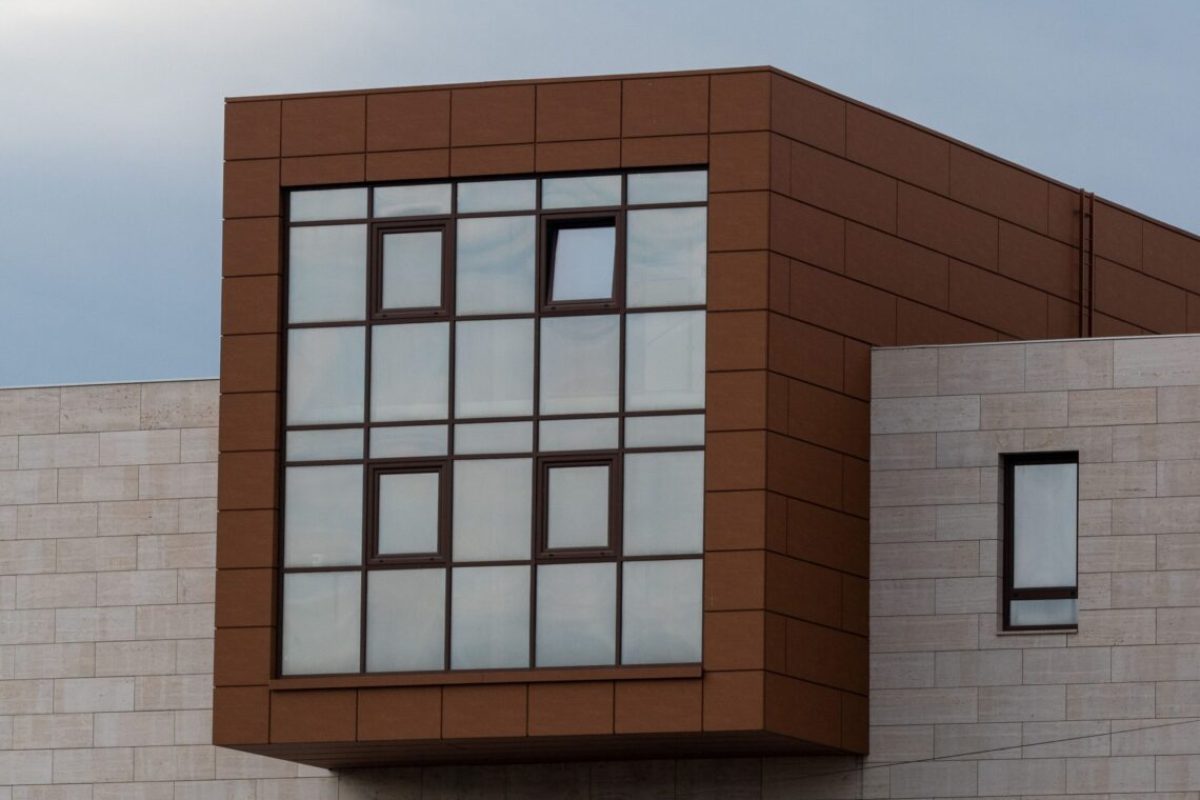 An image of a modern business building featuring a tall glass window bordering a brick wall