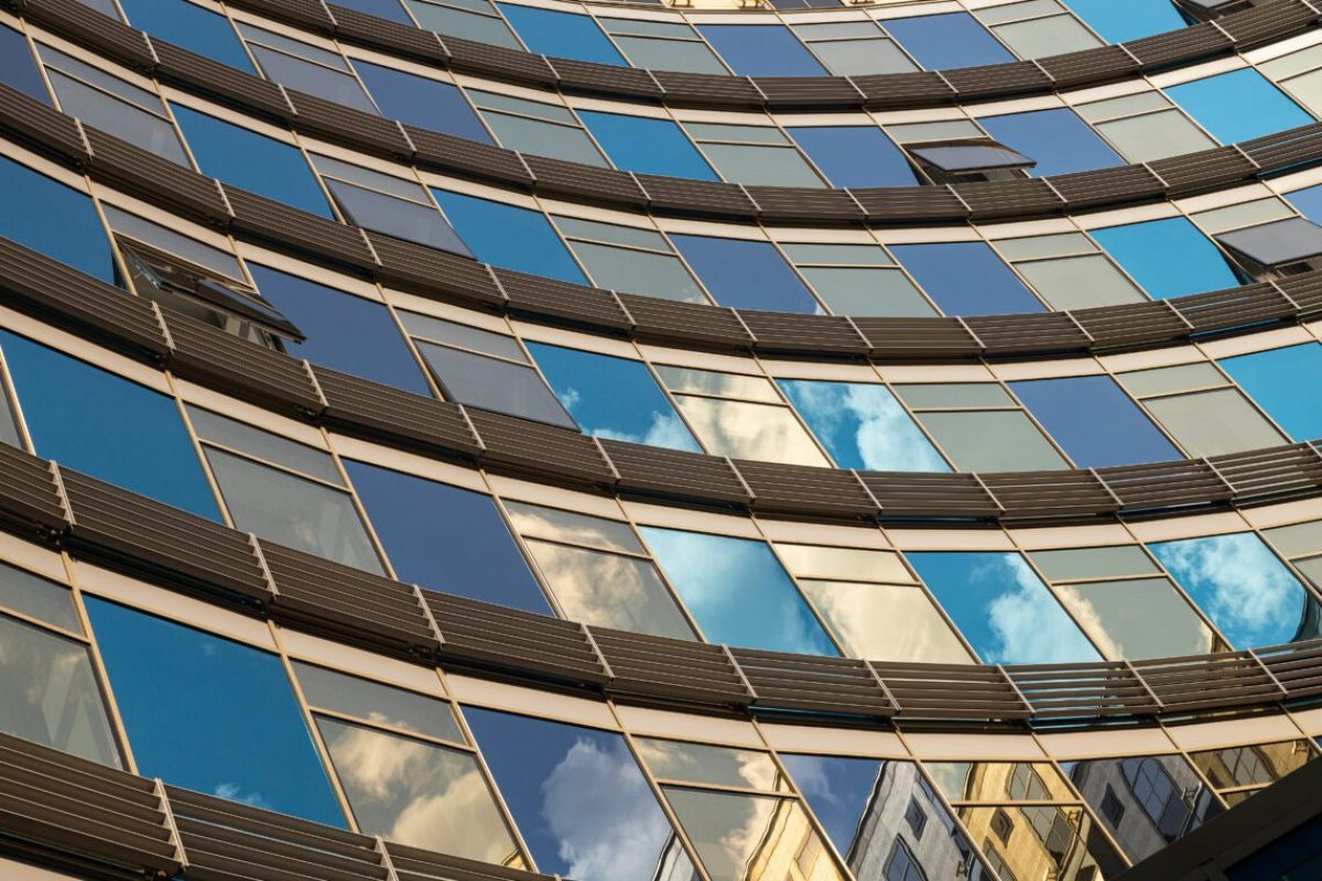 Closeup of glass wall of blue and golden shades with windows reflecting sky with clouds