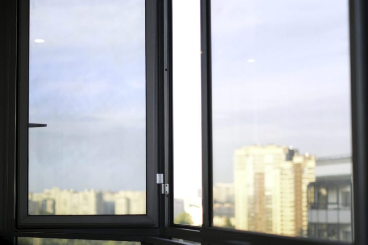 Close up of opened window with the blue cloudy sky and high rise buildings outside. Empty balcony of a residential building in the morning.