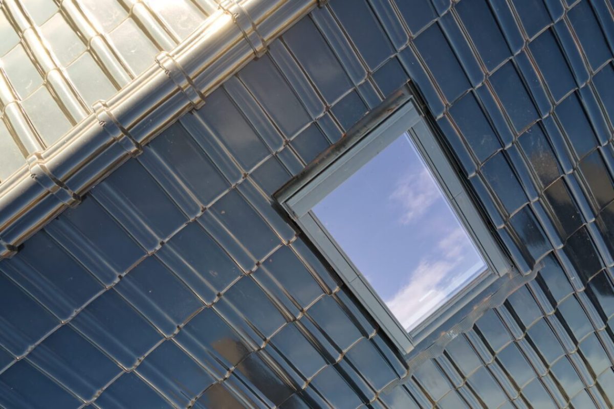 Closeup of attic window on house roof top covered with ceramic shingles. Tiled covering of building.