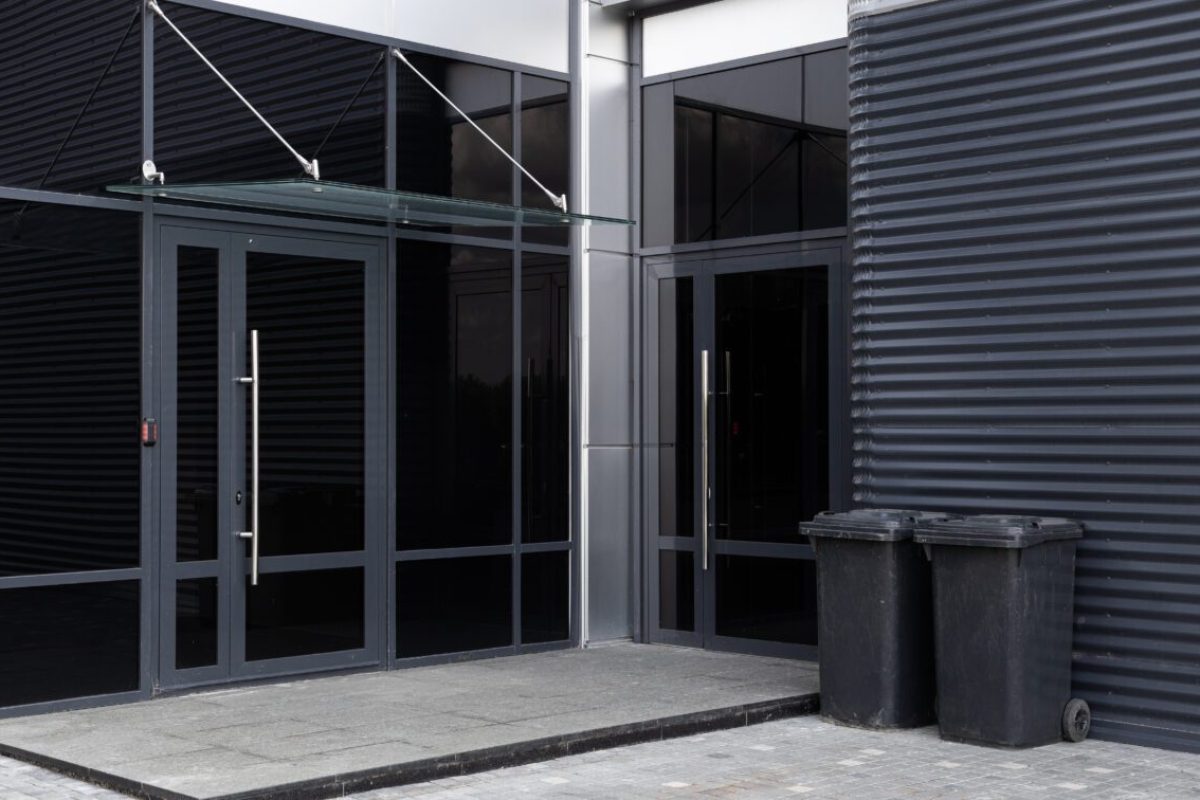 Glass doors - entrance to modern building and two scuffed black dustbins against black metal corrugated wall nearby