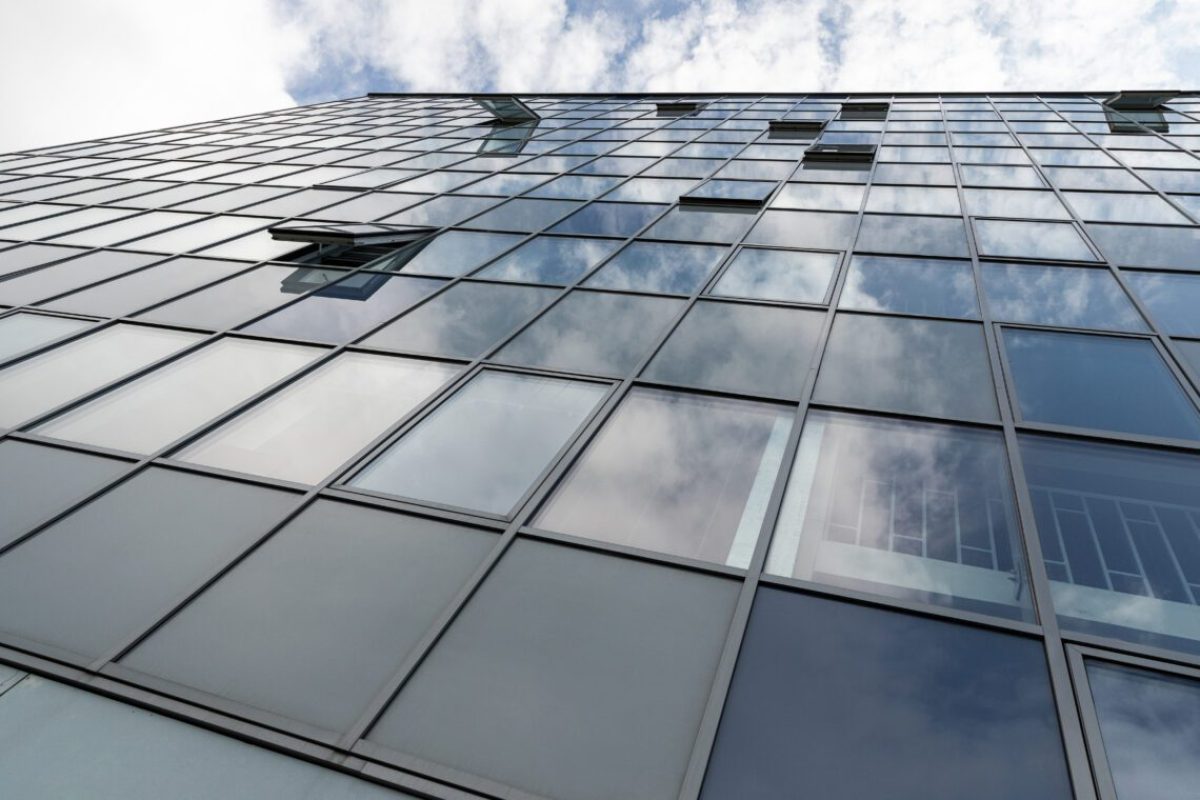 Ground view of tall business cenre facade with sky reflection