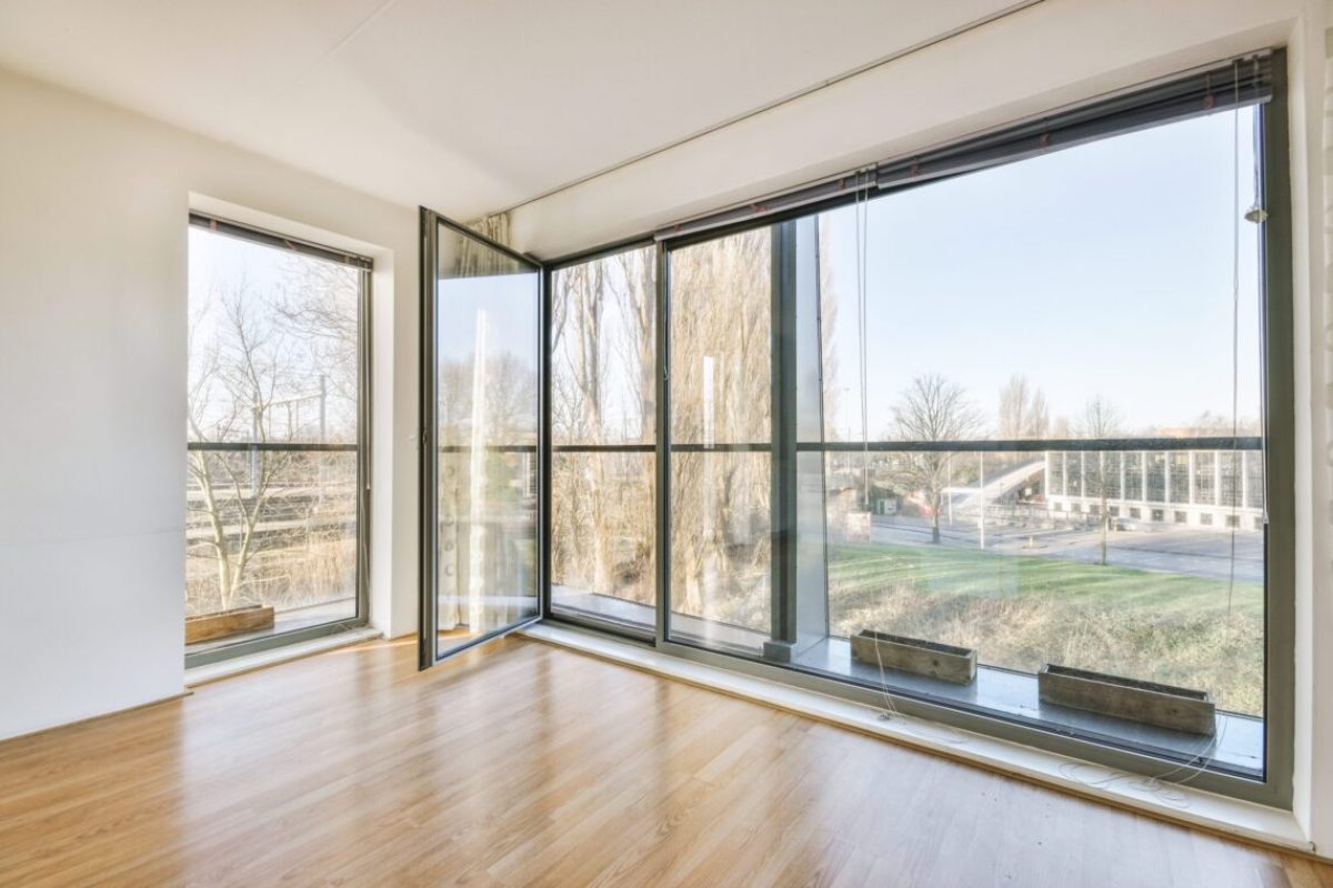 Interior of empty white room with large balcony windows with curtains and wooden parquet floor