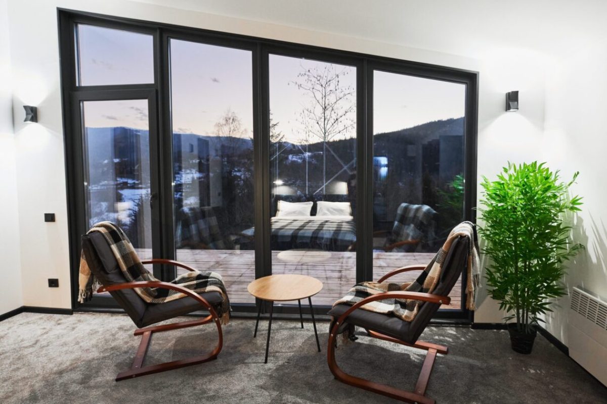 Light room with small coffee table and armchairs against large window with scenic view. Front view of living room with snowy mountain landscape through panoramic window at dusk. Concept of resting.