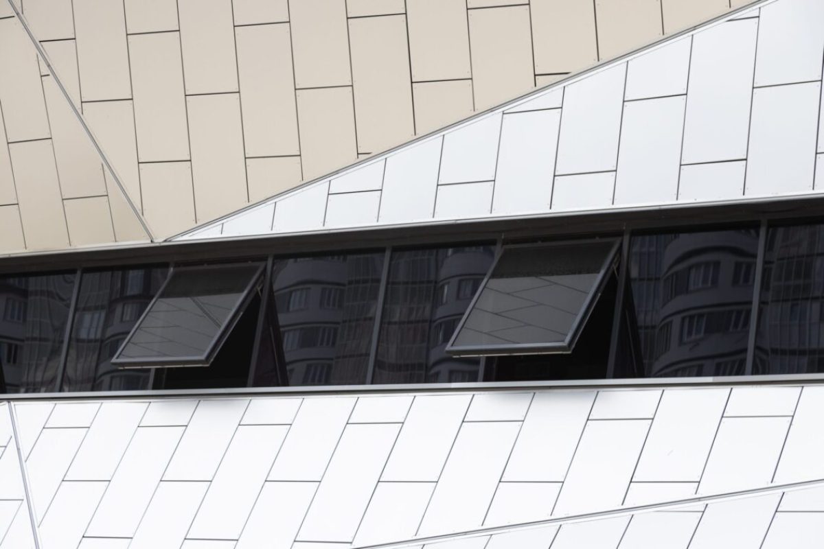 Outside view on white tiled wall of building with few black smoked windows opened