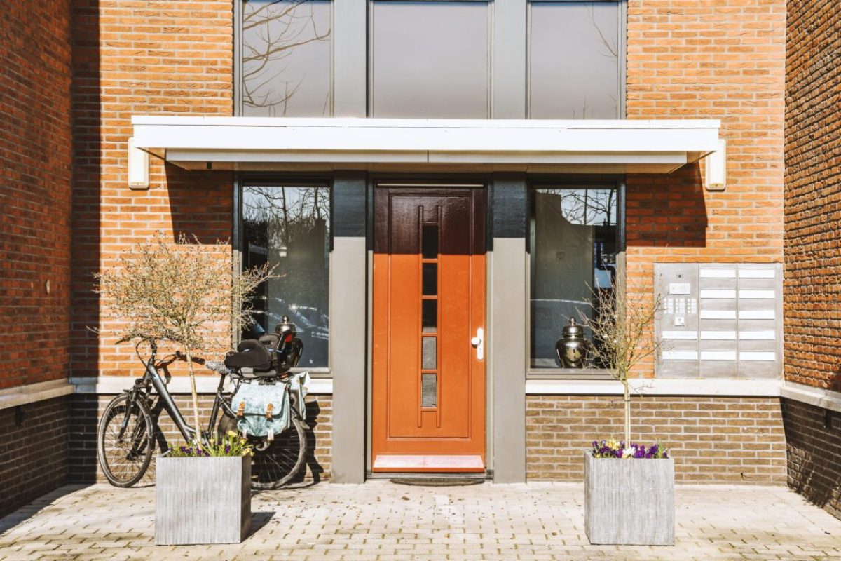 The front view of a brick building with signs, pavement and wooden doors lead to the apartment