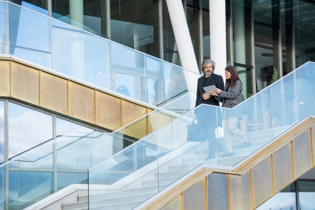 Young elegant brunette businesswoman with touchpad showing her male colleague online video containing ideas for new business project